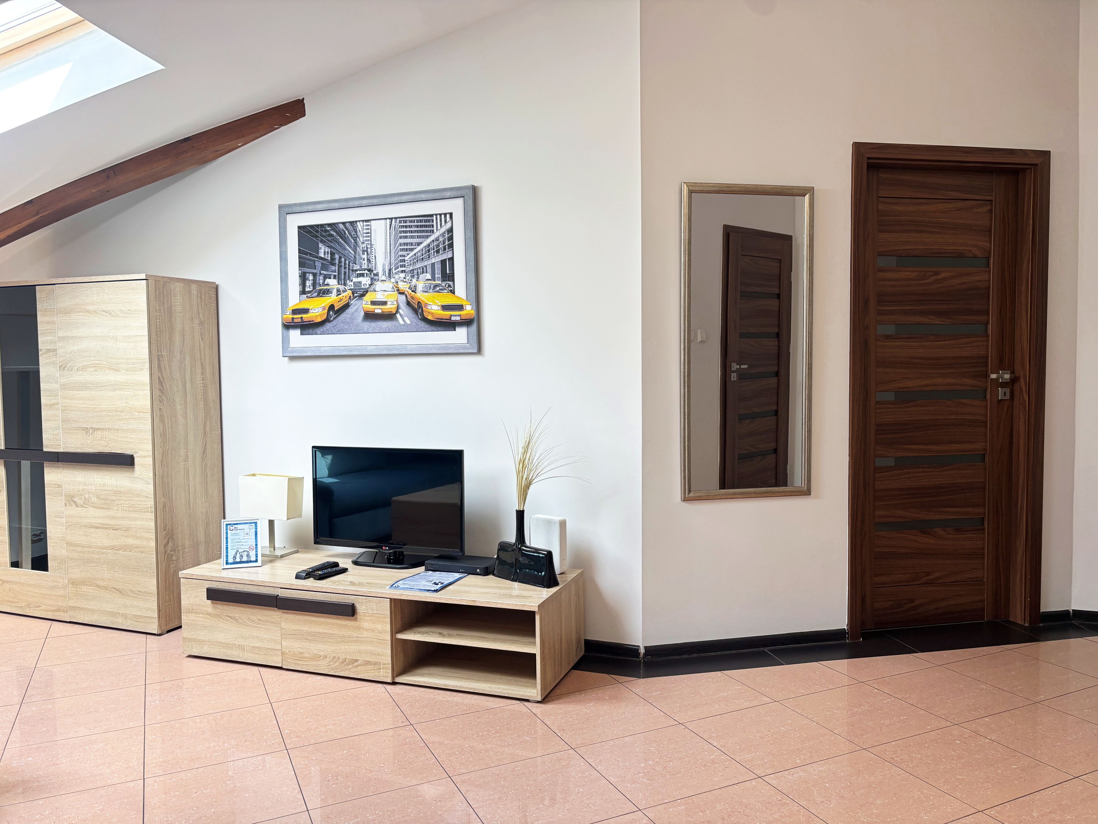 Un espace d’accueil avec un bureau en bois, un tableau encadré représentant des taxis, un miroir et une porte en bois.