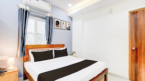 Un dormitorio con cama de madera, mesita de noche, lámpara, ventana con cortinas y aire acondicionado instalado en la pared.