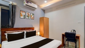 Una habitación de hotel con una cama, un armario, un escritorio con una silla y un equipo de aire acondicionado.