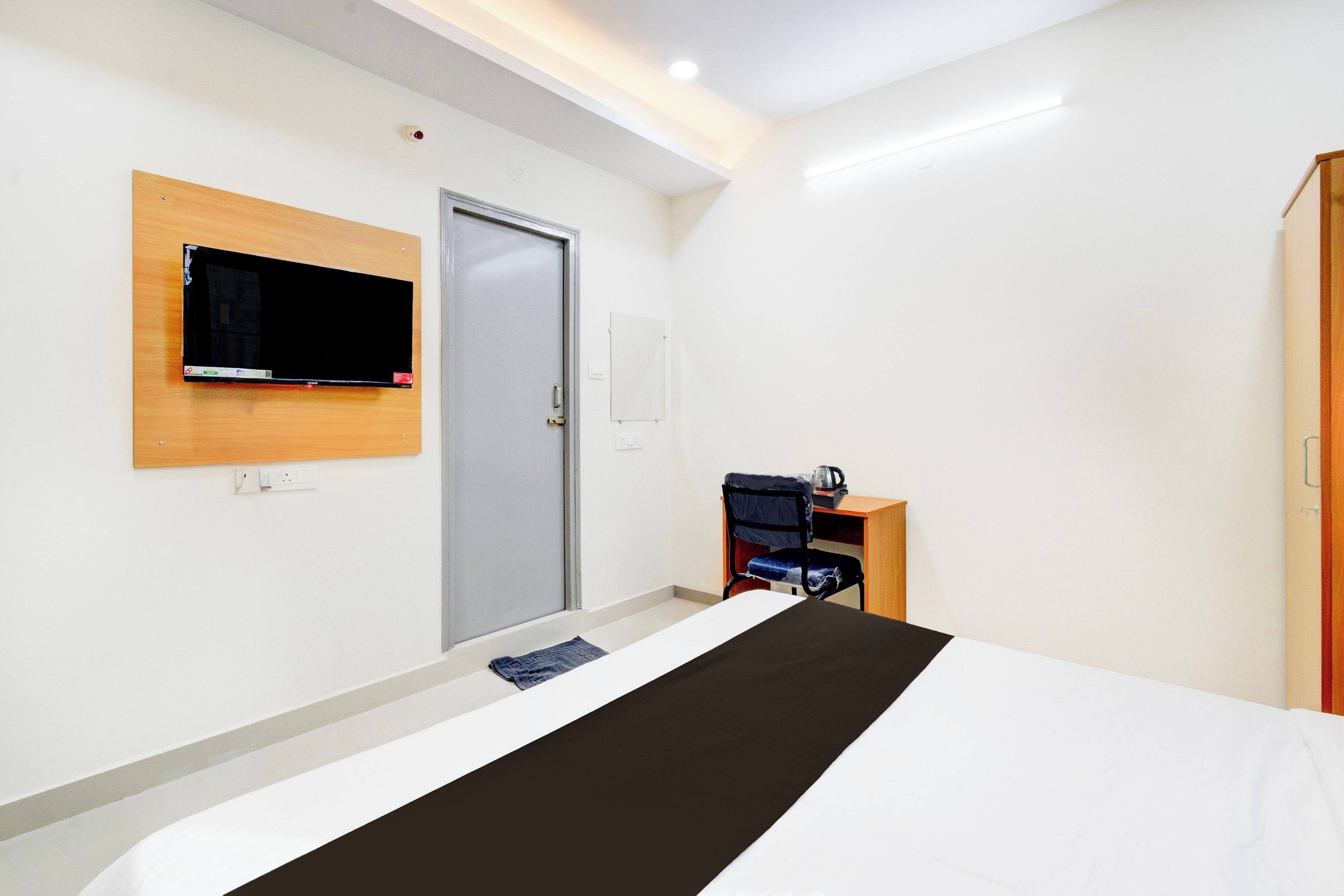 A hotel room with a bed, a television mounted on the wall, a door, and a small desk with a chair.