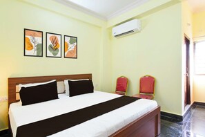 Habitación de hotel con cama, dos sillas, equipo de aire acondicionado y tres cuadros en la pared.