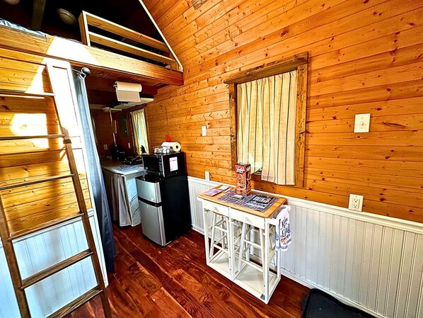 A compact kitchen with wooden walls, a refrigerator, a microwave, and a small dining table.