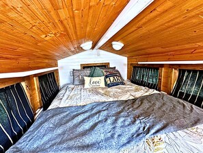 Un dormitorio con techo de madera, cama con ropa de cama estampada y una ventana con cortinas.