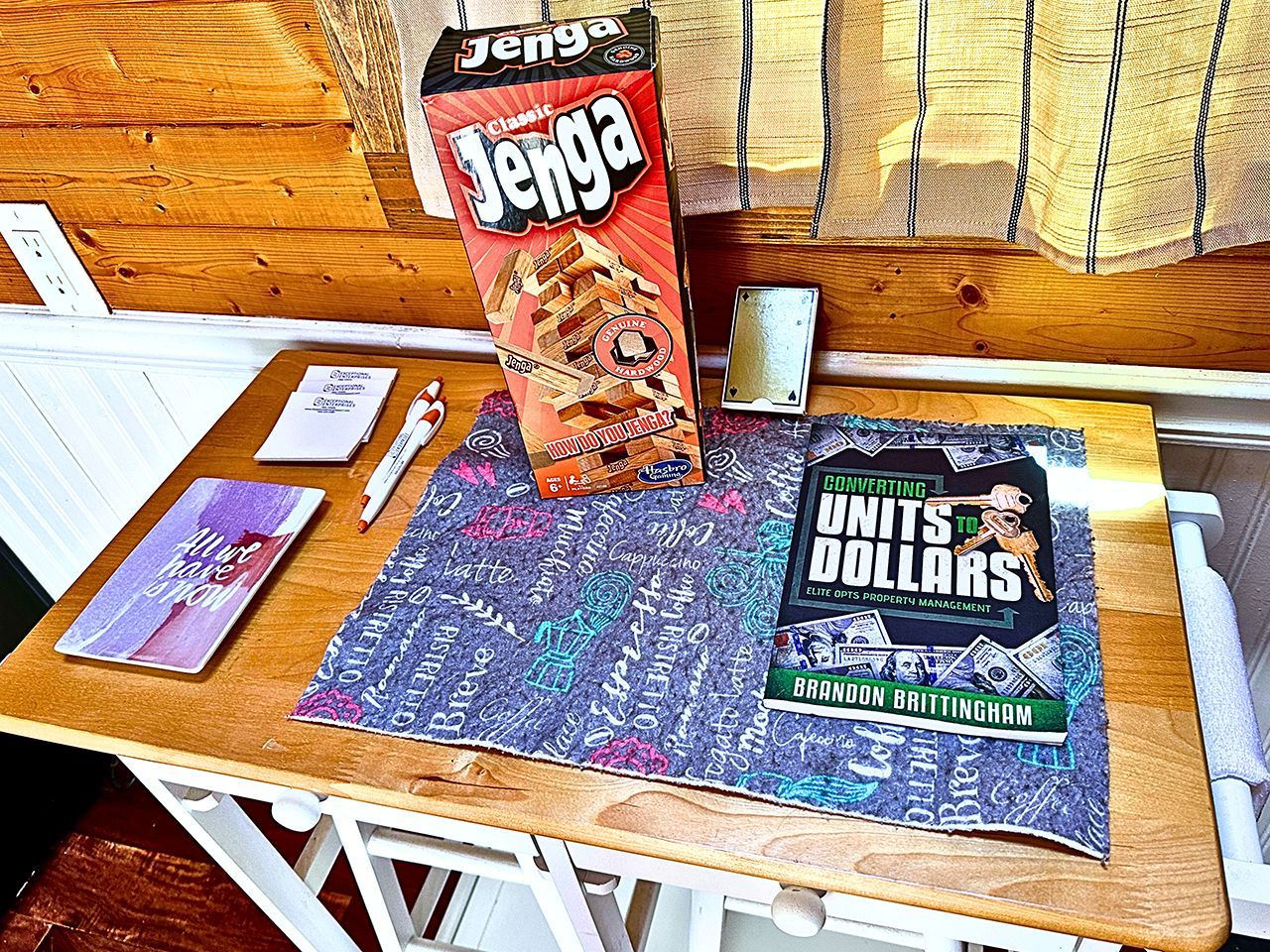 Una mesa de madera con una caja de Jenga, un cuaderno, un bolígrafo y un libro titulado 'Converting Units to Dollars'.