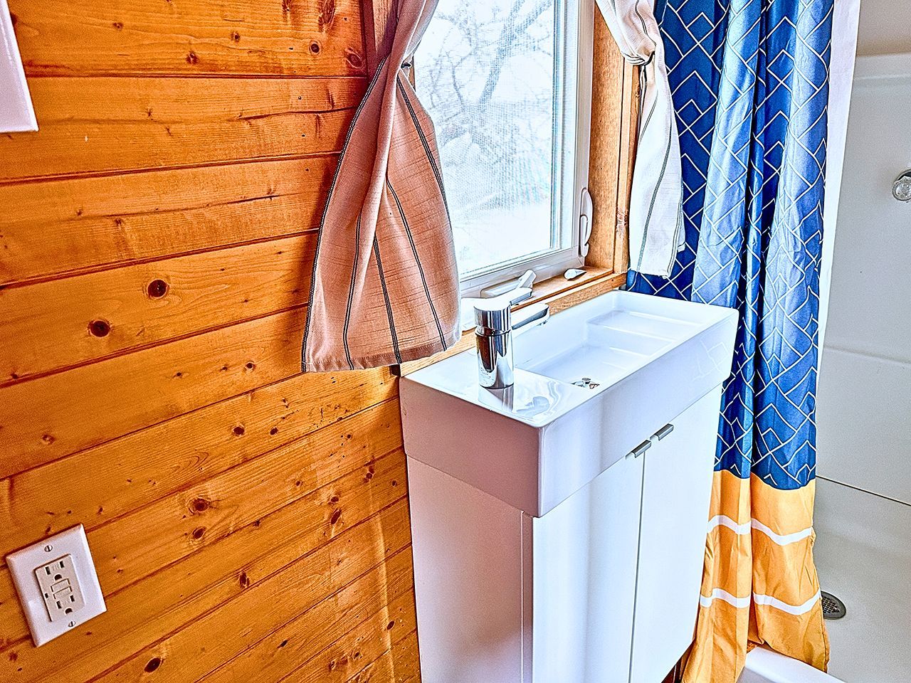 Ein Badezimmer mit einer Holzwand, einem weißen Waschbecken und einem Fenster mit Vorhängen.