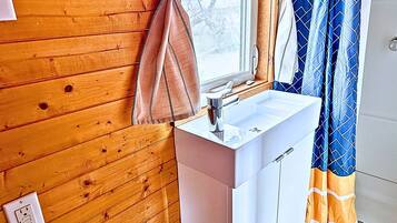 Ein Badezimmer mit einer Holzwand, einem weißen Waschbecken und einem Fenster mit Vorhängen.