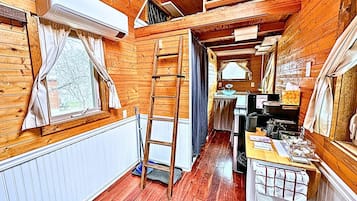 A wooden interior with a kitchen area, a ladder, and a window with curtains.