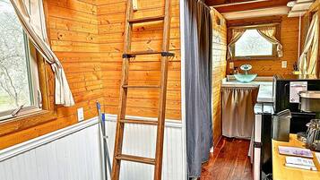Interior de una cabaña de madera con una escalera, una ventana, un lavamanos y un refrigerador.