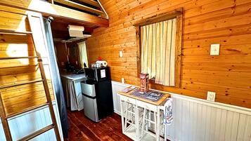 A compact kitchen with wooden walls, a refrigerator, a microwave, and a small dining table.