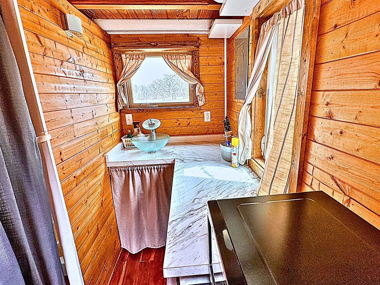 A narrow cabin with a wooden interior, a small sink, and a window with curtains.
