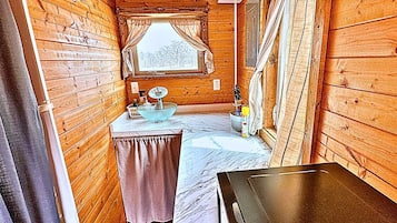 A narrow cabin with a wooden interior, a small sink, and a window with curtains.