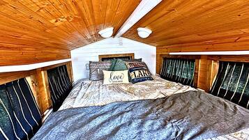 A bedroom with a wooden ceiling, a bed with patterned bedding, and a window with curtains.