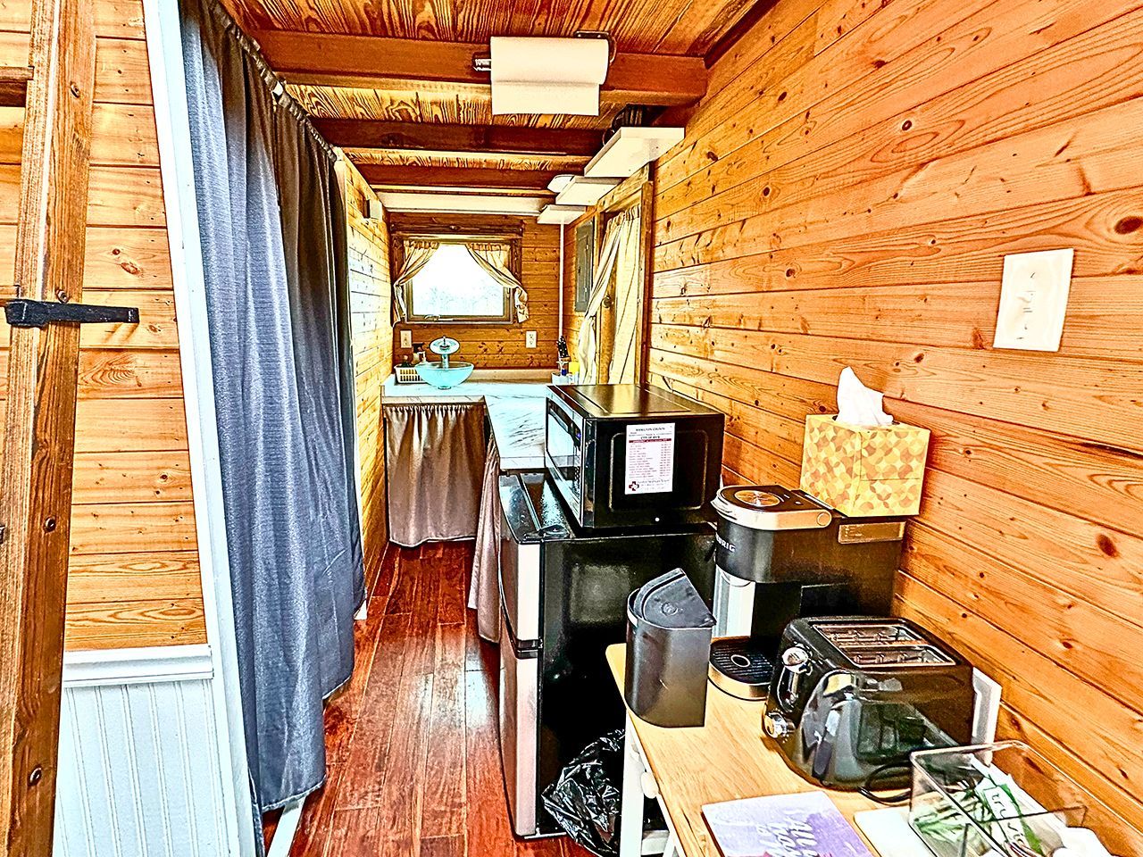 A compact kitchen with wooden walls, a microwave, a toaster, and a sink.