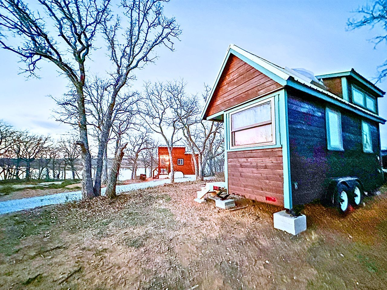 Una cabaña pequeña con un garaje, rodeada de árboles y una masa de agua.