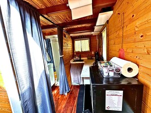 A narrow hallway with wooden walls, a kitchen area with a sink and countertop, and a window with curtains.