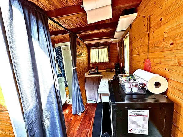 A narrow hallway with wooden walls, a kitchen area with a sink and countertop, and a window with curtains.