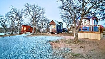 A rural property with a gravel driveway, a small wooden cabin, and a larger house with a fenced yard.