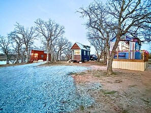 Una propiedad rural con camino de grava, una cabaña de madera pequeña y una casa más grande con patio cercado.