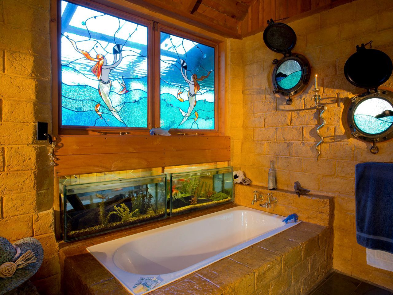 Een badkamer met een groot bad, een vissenkom en een raam met glas-in-loodafbeeldingen van zeemeerminnen.