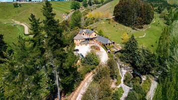 Une grande maison dotée d’une allée spacieuse et d’une pelouse bien entretenue, entourée d’arbres denses et de collines ondulantes.