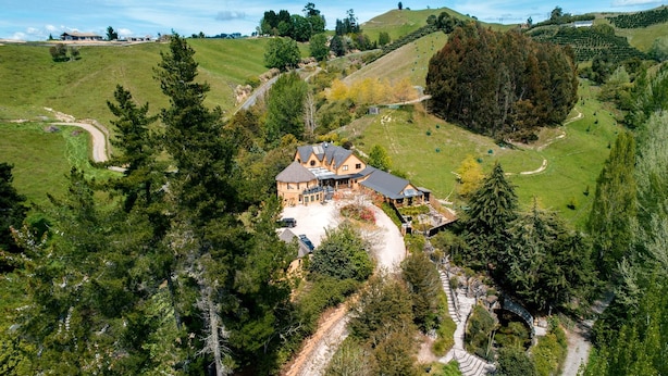 A large house with a spacious driveway and a well-maintained lawn, surrounded by dense trees and rolling hills. - Luxury Castle for Large Groups in Nelson, New Zealand (Upper Moutere)