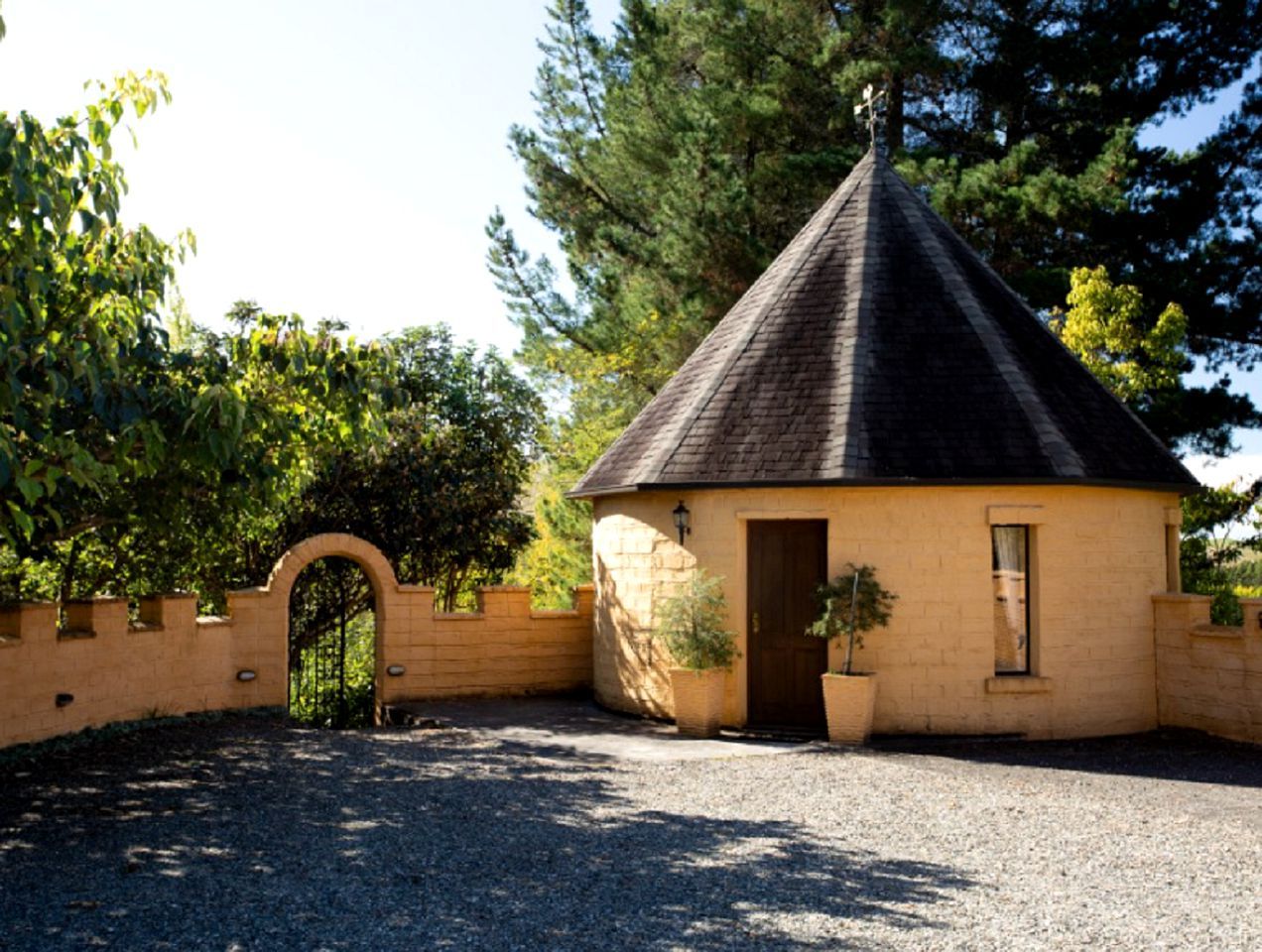 A small, single-story building with a conical roof, a brick entrance, and a gravel driveway.