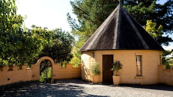 A small, single-story building with a conical roof, a brick entrance, and a gravel driveway.
