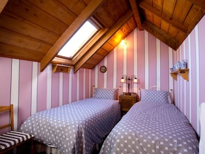 A bedroom with two beds, a skylight, and a wooden ceiling.