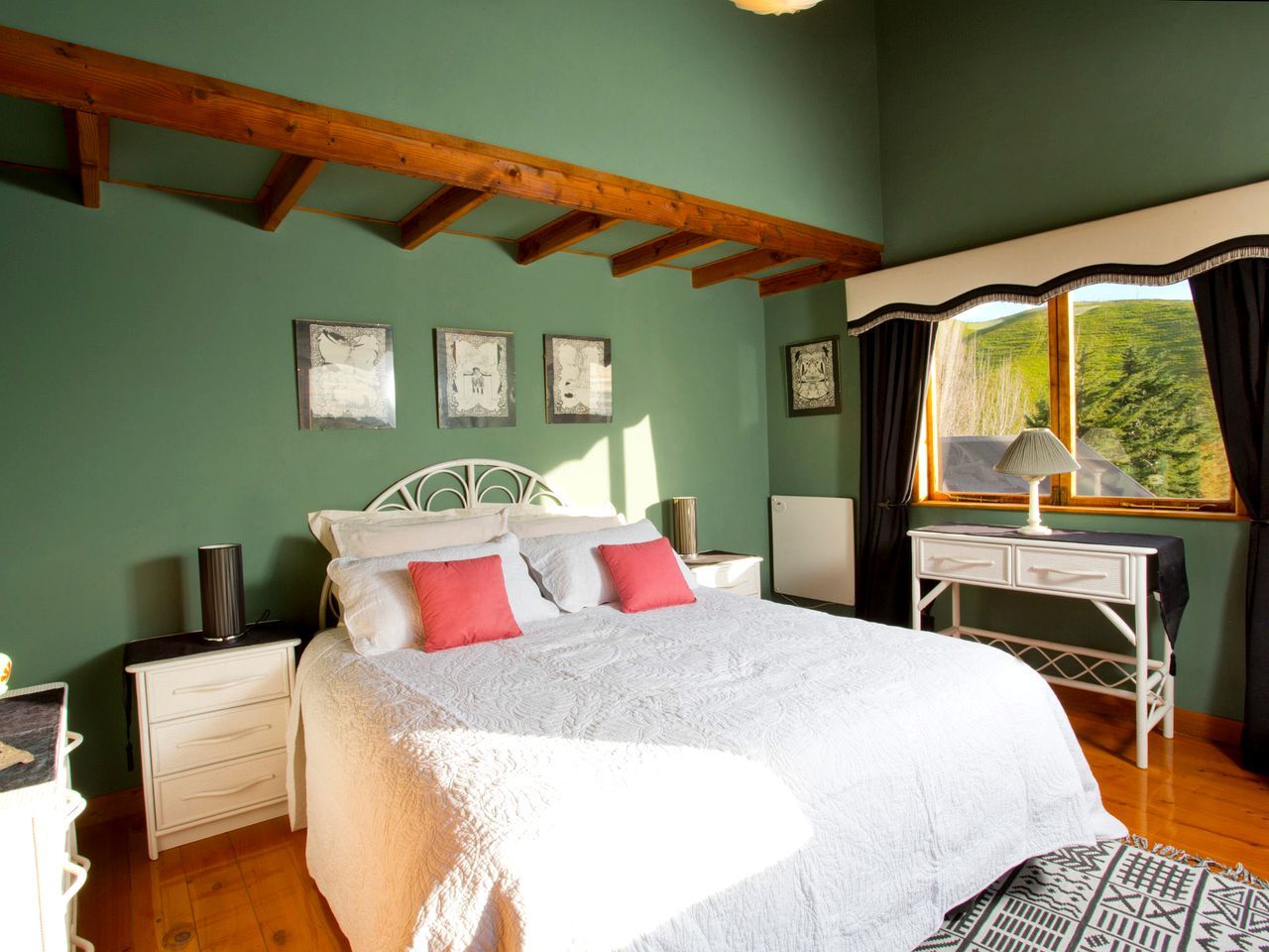 Une chambre à coucher avec un lit, des tables de chevet, un bureau et une fenêtre avec des rideaux.