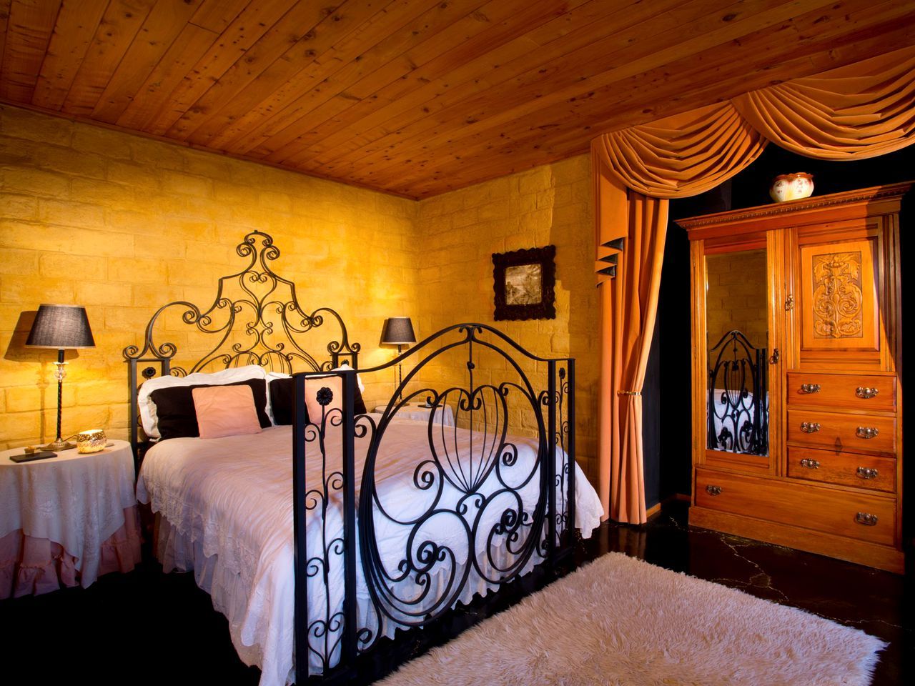Une chambre à coucher avec un plafond en bois, un lit avec un cadre en métal, une table de chevet, une commode et un miroir.