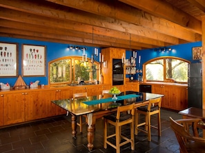 A wooden kitchen with a glass-top dining table, wooden cabinets, and a window overlooking greenery.
