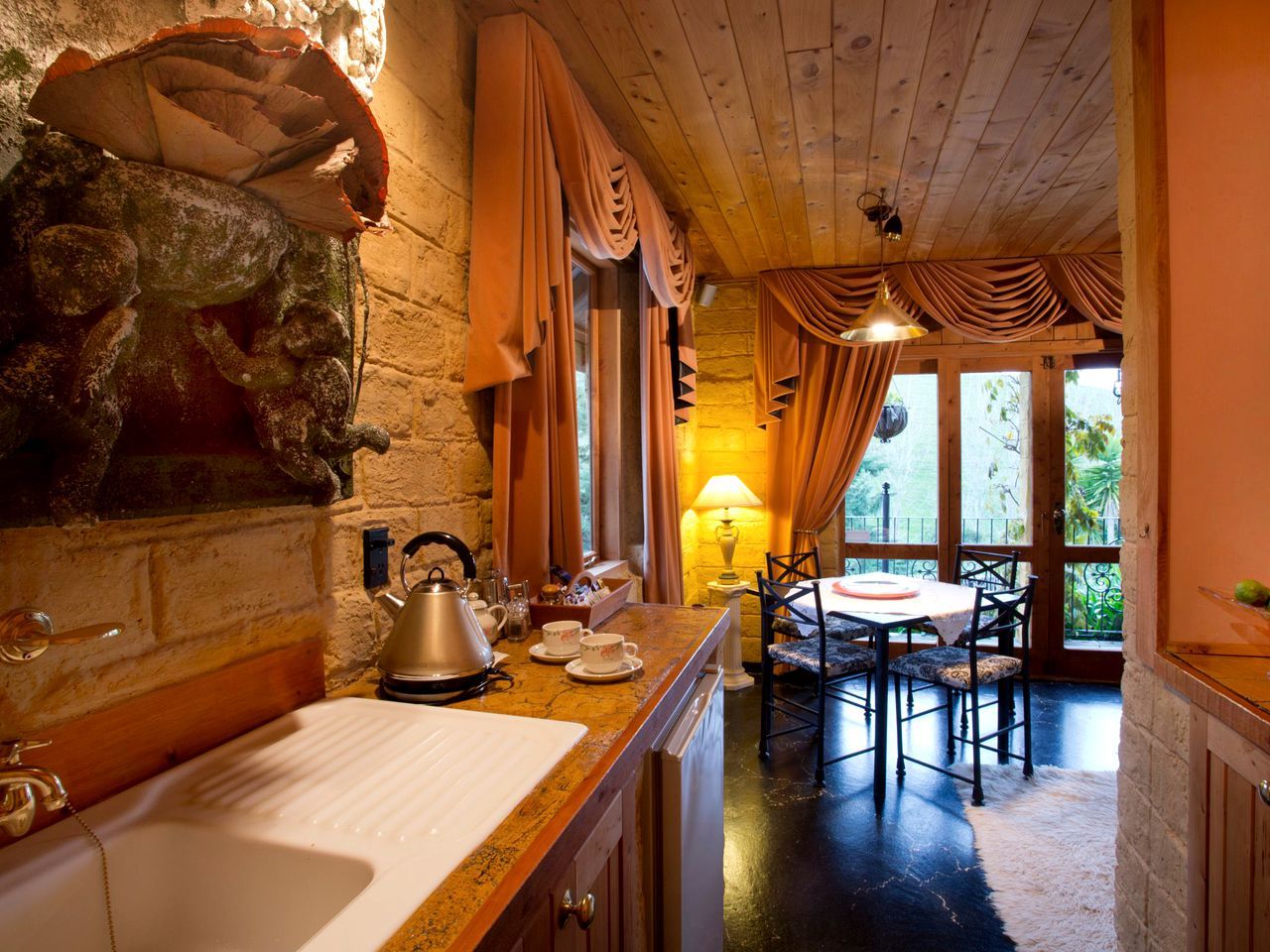 A rustic kitchen with a stone wall, wooden cabinets, and a dining area with a table and chairs.