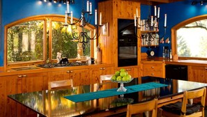 A wooden kitchen with a large island, a dining table, and a view of greenery outside. - Luxury Castle for Large Groups in Nelson, New Zealand (Upper Moutere)