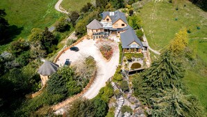 A large house with a spacious driveway, surrounded by lush greenery and trees. - Luxury Castle for Large Groups in Nelson, New Zealand (Upper Moutere)