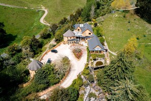 A large house with a spacious driveway, surrounded by lush greenery and trees. - Luxury Castle for Large Groups in Nelson, New Zealand (Upper Moutere)