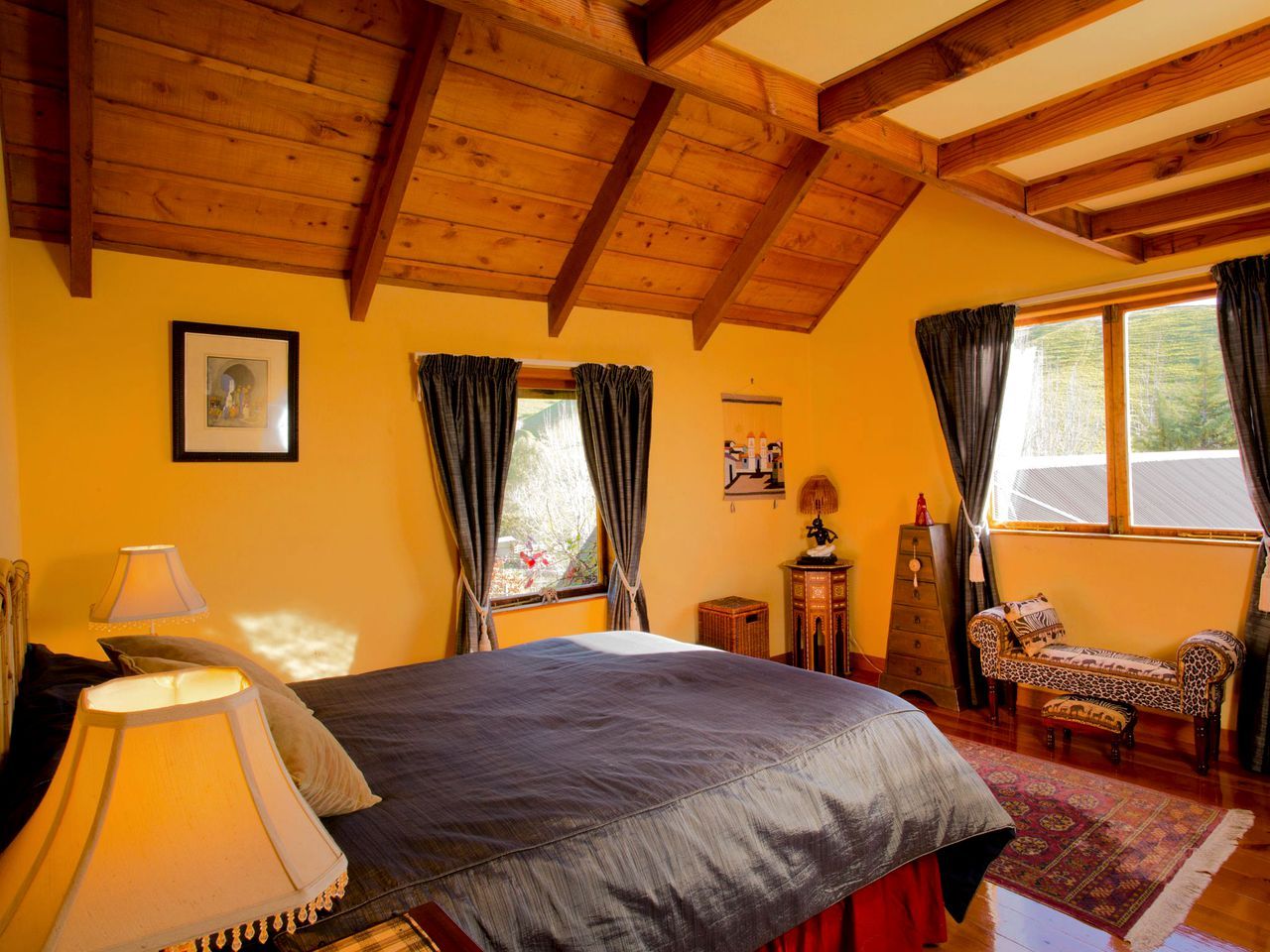 A bedroom with a bed, a nightstand, a lamp, a dresser, a chair, and a window with curtains.