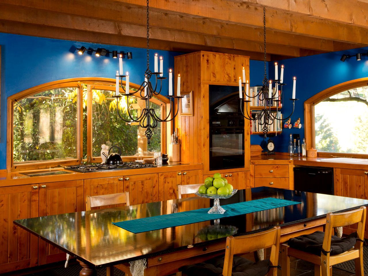 A wooden kitchen with a large island, a dining table, and a view of greenery outside.