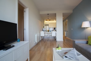 En moderne stue med et fladskærms-tv, et sofabord med aviser, en sofa og et spiseområde med stole og et bord.