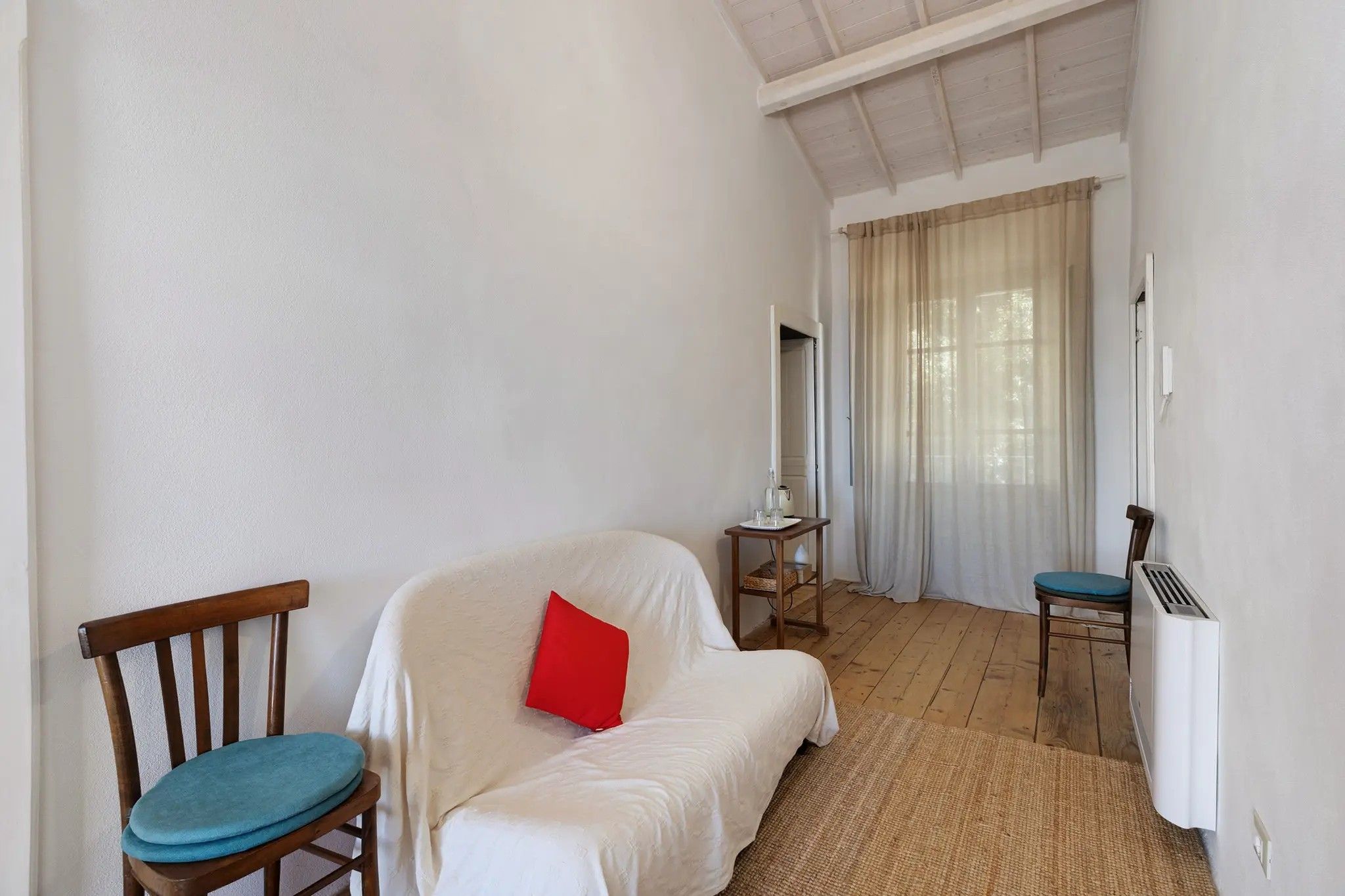 Ein Zimmer mit einem Bett, einem Sessel, einem Tisch mit Lampe und einer Heizung.