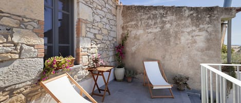 A balcony with a stone wall, a window, and a table with chairs.
