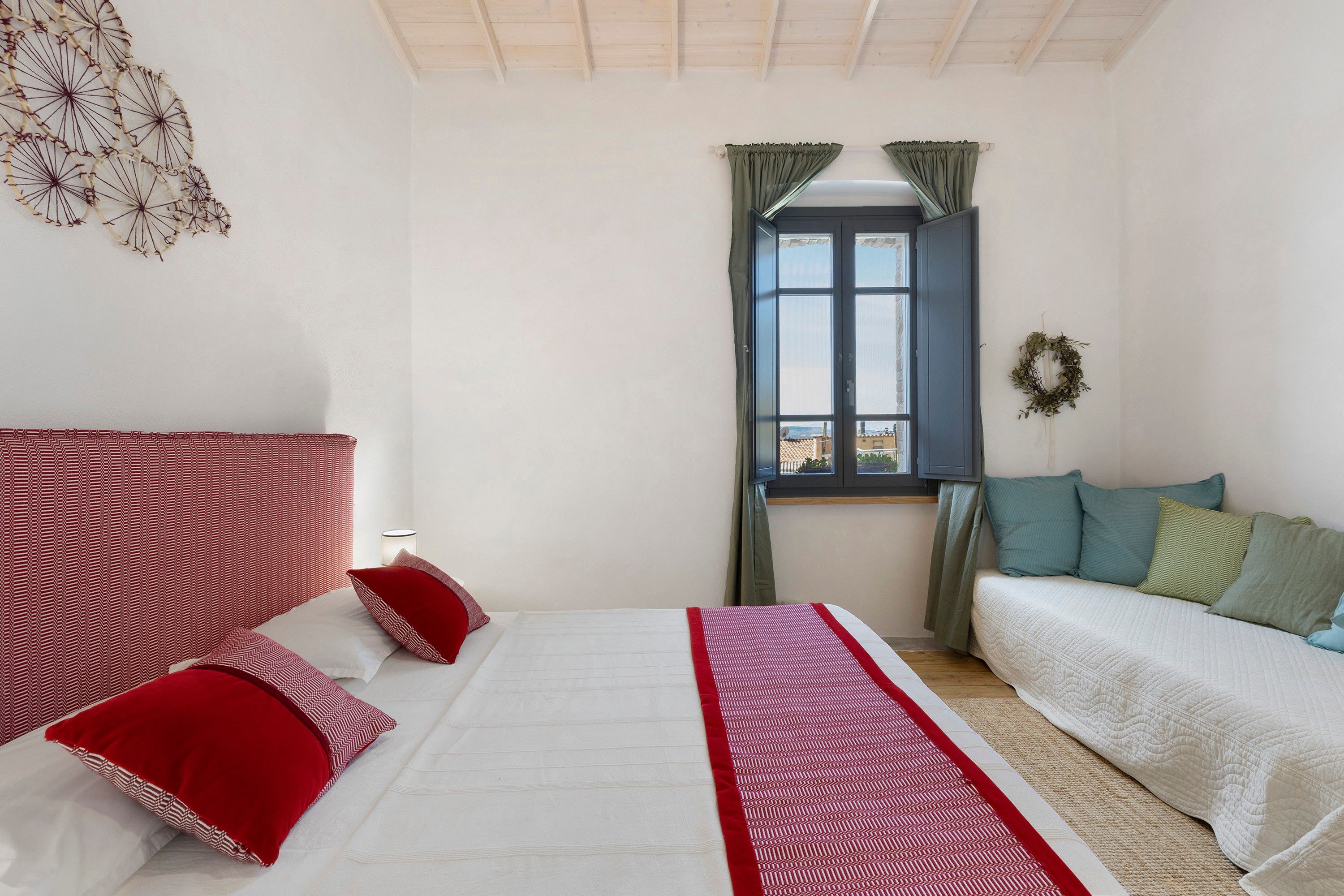 Una camera da letto con un letto, un divano, una finestra con tende e un elemento decorativo a parete.