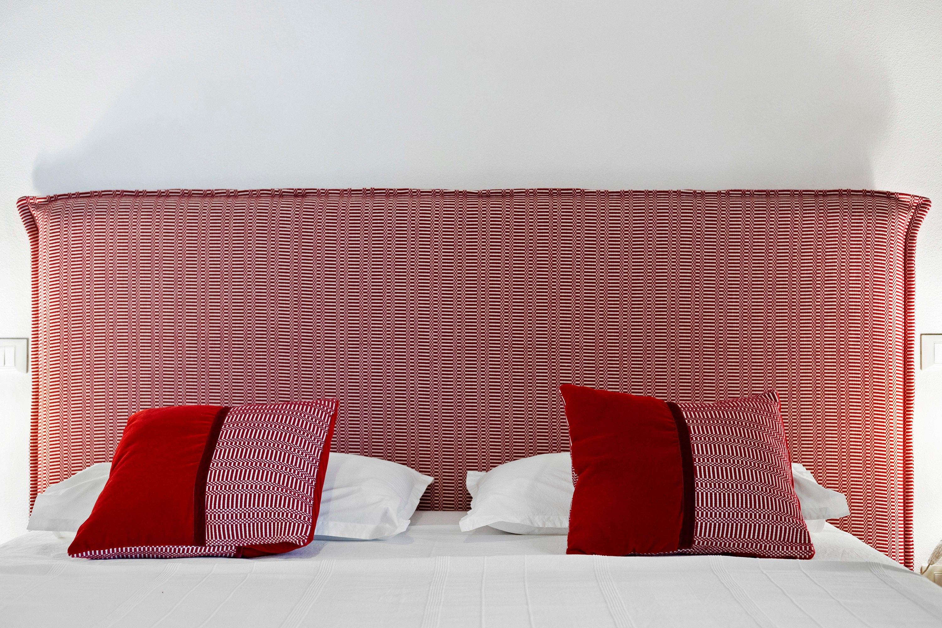 Ein Bett mit einem roten und weißen Kopfstück, weißer Bettwäsche und zwei roten Kissen.