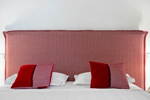 A bed with a red and white patterned headboard, white bedding, and two red pillows.