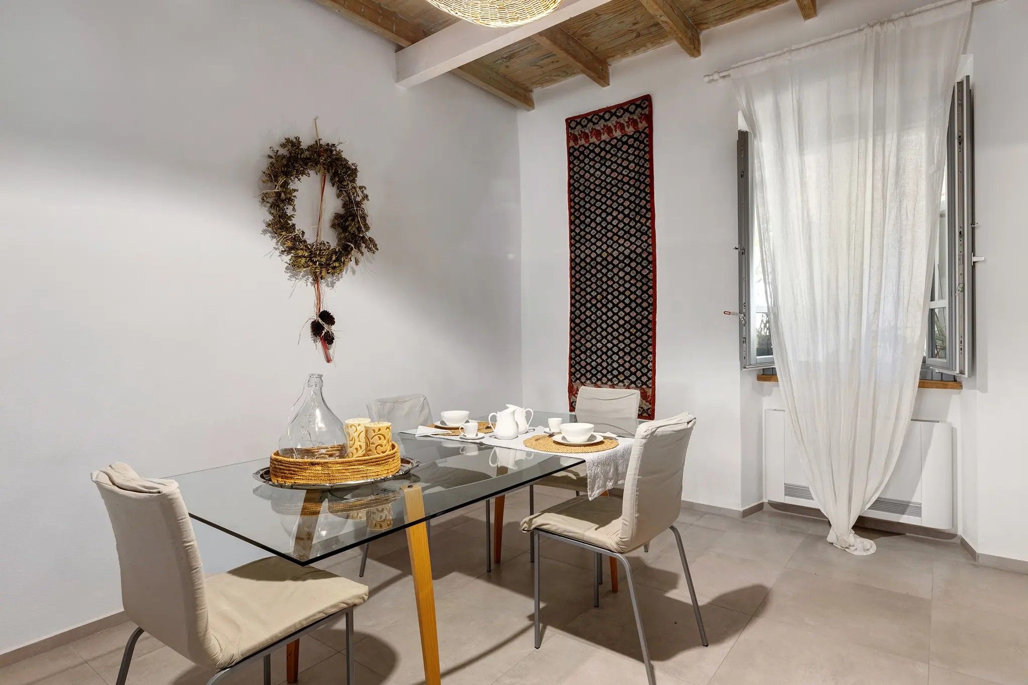 Un'area pranzo con un tavolo in vetro, sedie bianche, una ghirlanda decorativa e una tenda a fantasia.
