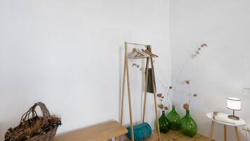 Una stanza con una panca di legno, uno stendibiancheria, un cesto e un tavolo con una lampada.