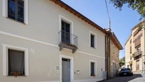 Edifici de dues plantes amb un balcó, una porta i una finestra amb cortina.