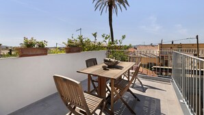 Terrassa exterior amb taula i cadires de fusta, envoltada de plantes en testos i una palmera.
