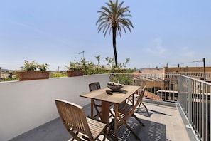 An outdoor patio with a wooden table and chairs, surrounded by potted plants and a palm tree.
