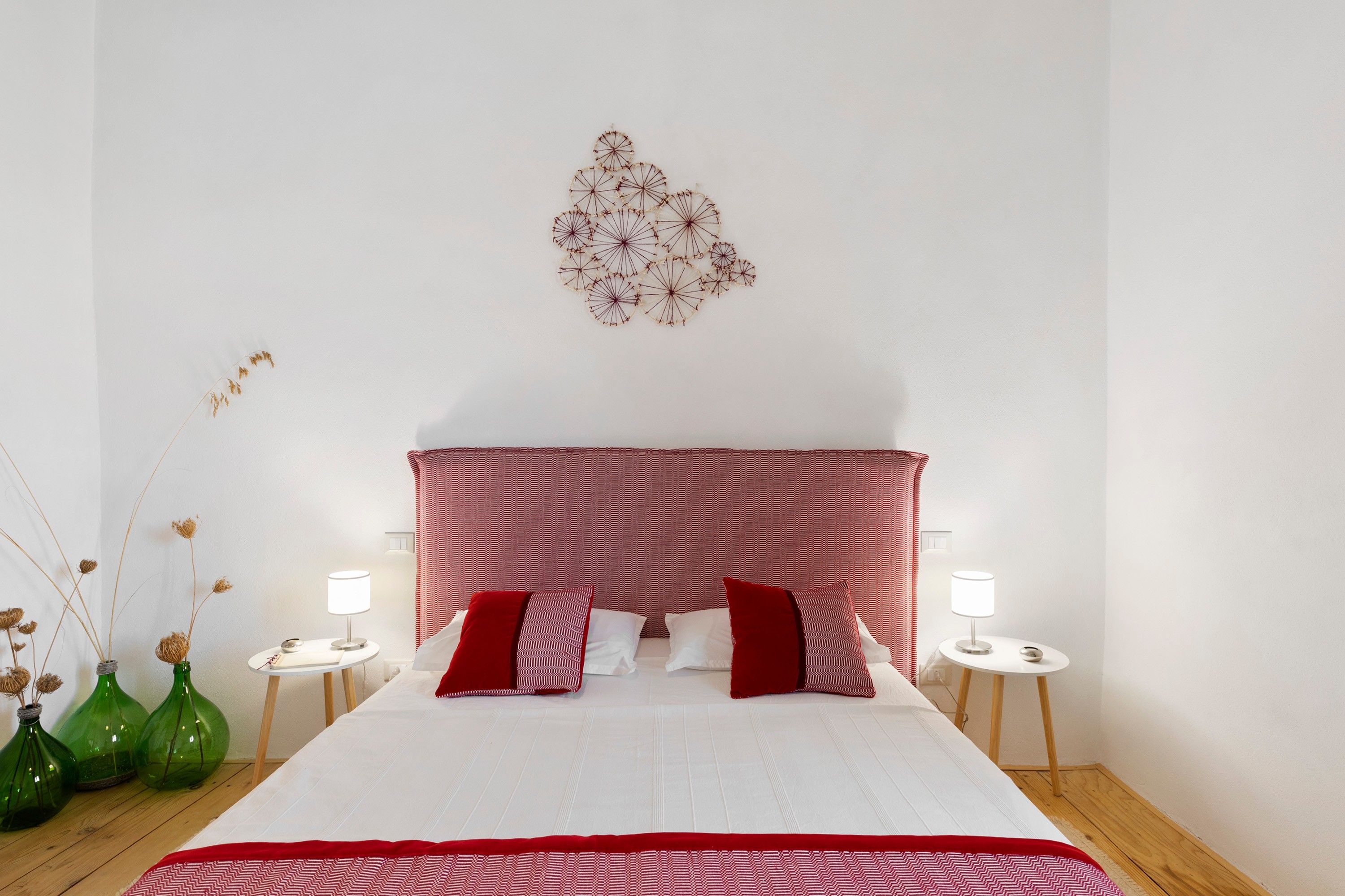 A hotel room with a bed, two bedside tables, a red and white patterned headboard, and decorative wall art.