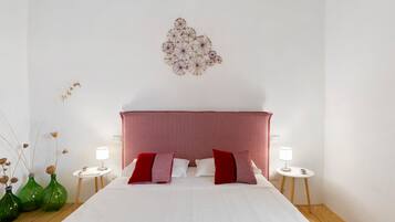 A hotel room with a bed, two bedside tables, a red and white patterned headboard, and decorative wall art.